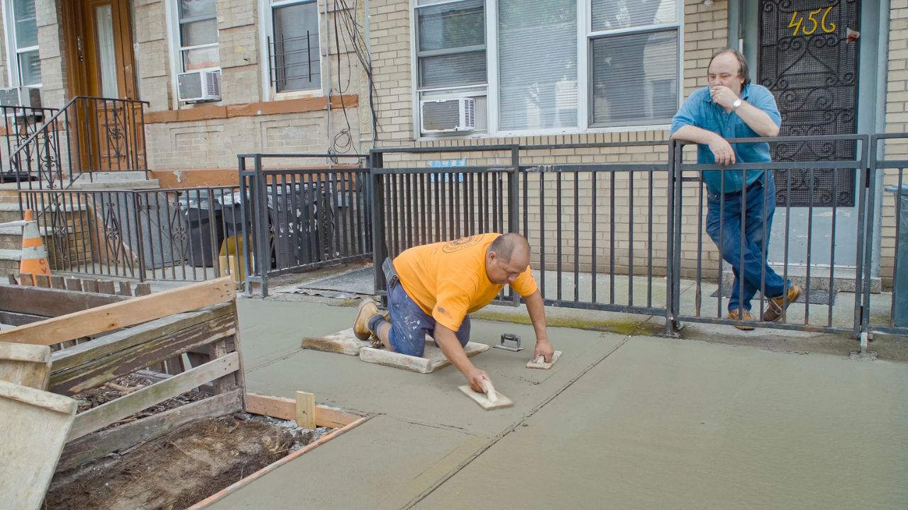 a man smoking while another puts down concrete